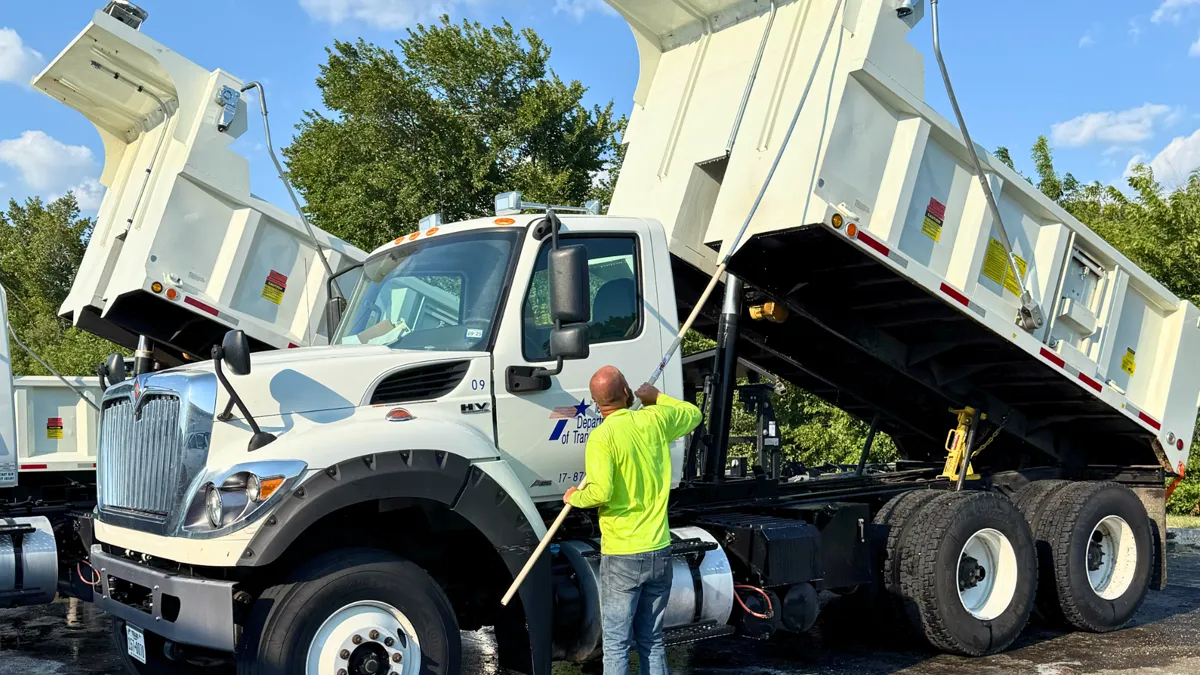Crew member washing down a dump truck under a maintenance program